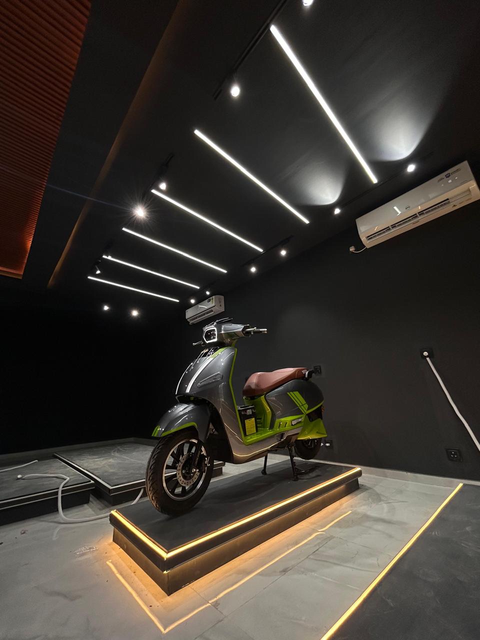 Dark themed EV showroom interior with a single electric scooter on a gold lit podium