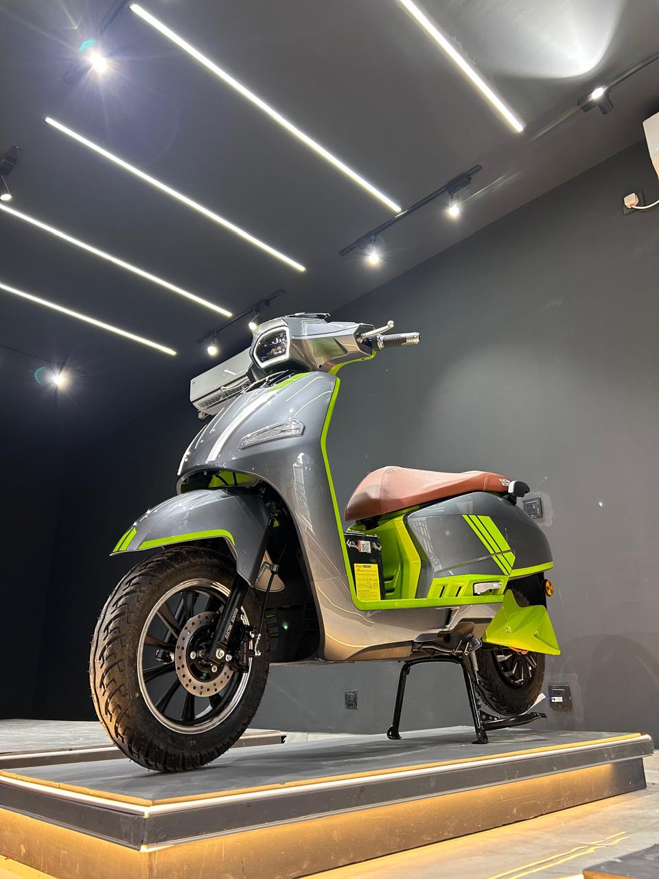 Grey and lime green premium electric scooter on a lit showroom display podium
