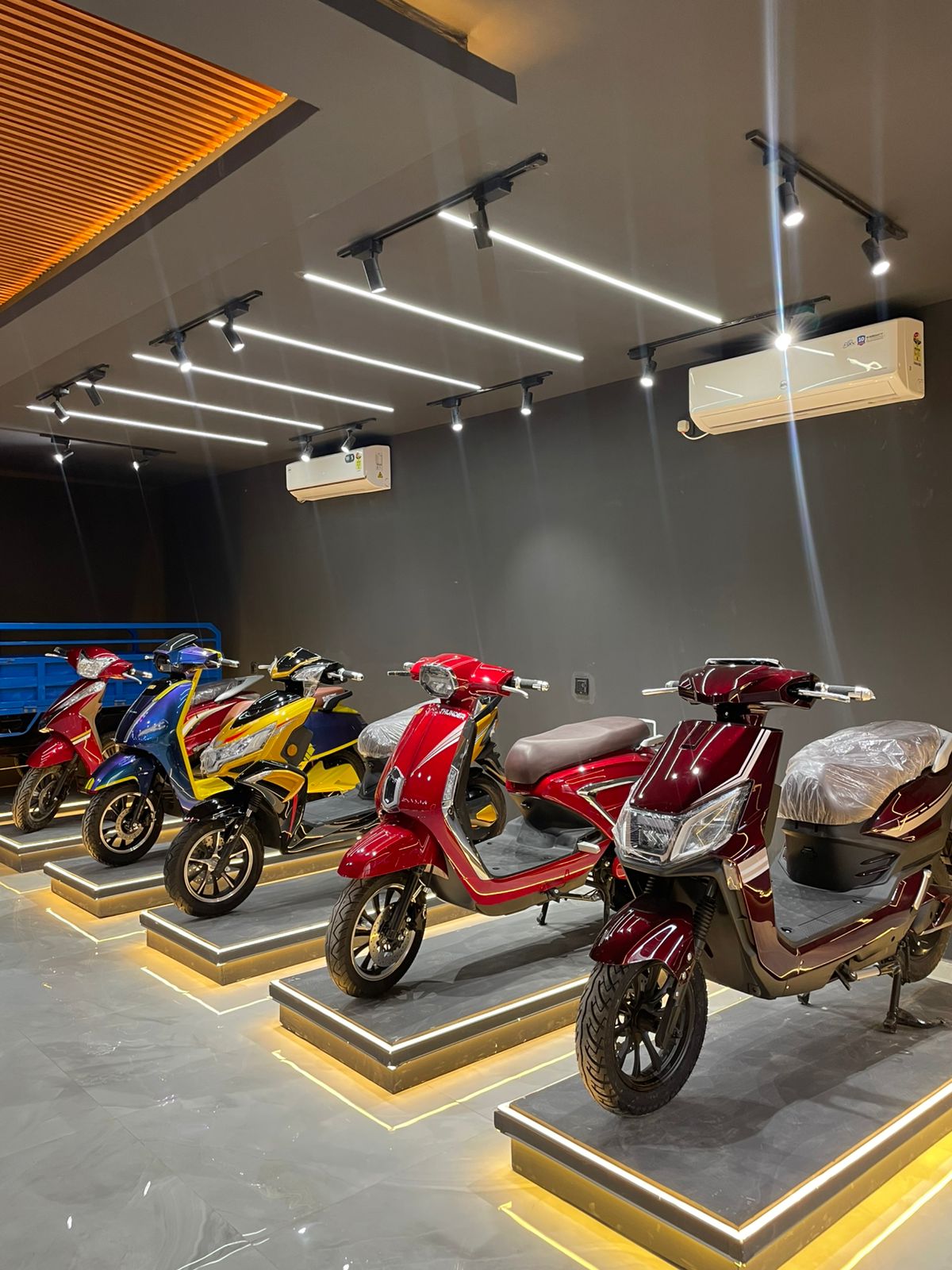 Row of electric two-wheelers displayed on illuminated podiums in a modern EV showroom